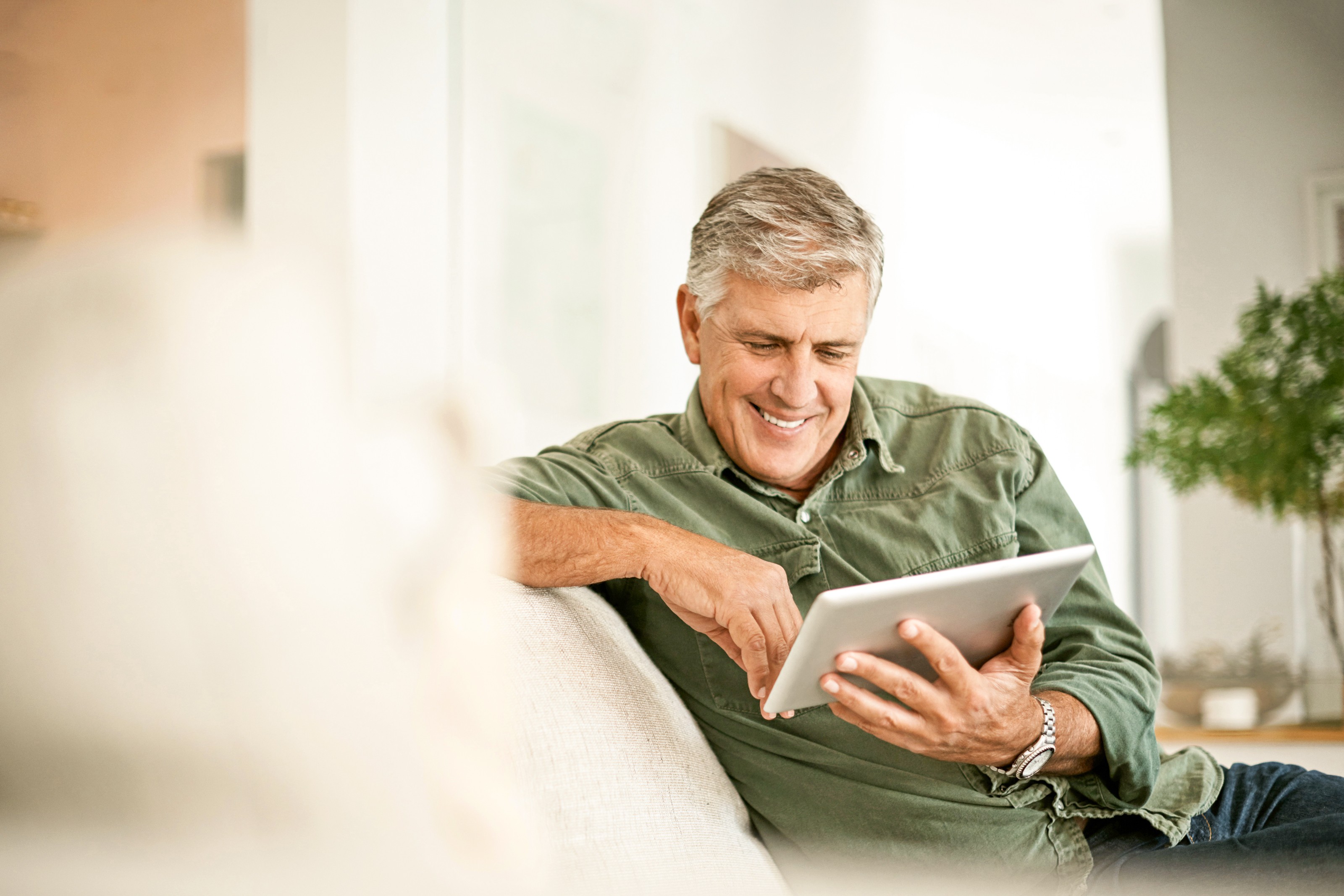 Junge Frau sitzt am Schreibtisch und schaut lächelnd auf ihr Tablet