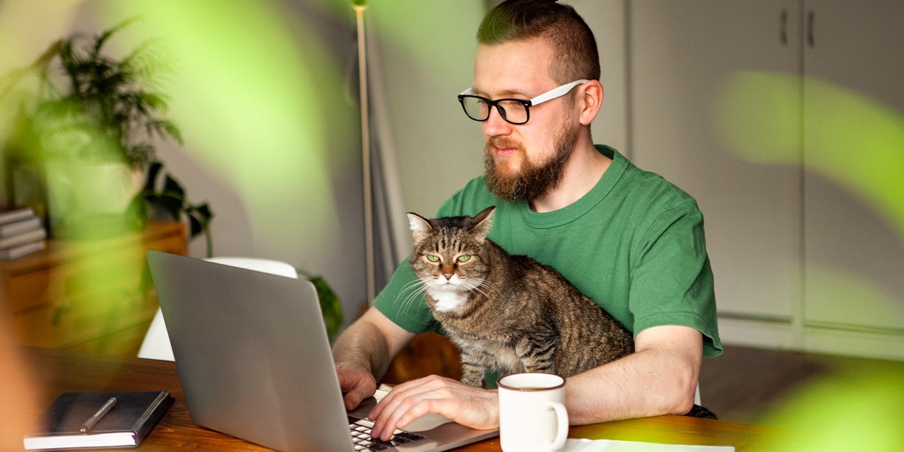 Mann sitzt mit Katze und Kaffeebecher vor Laptop