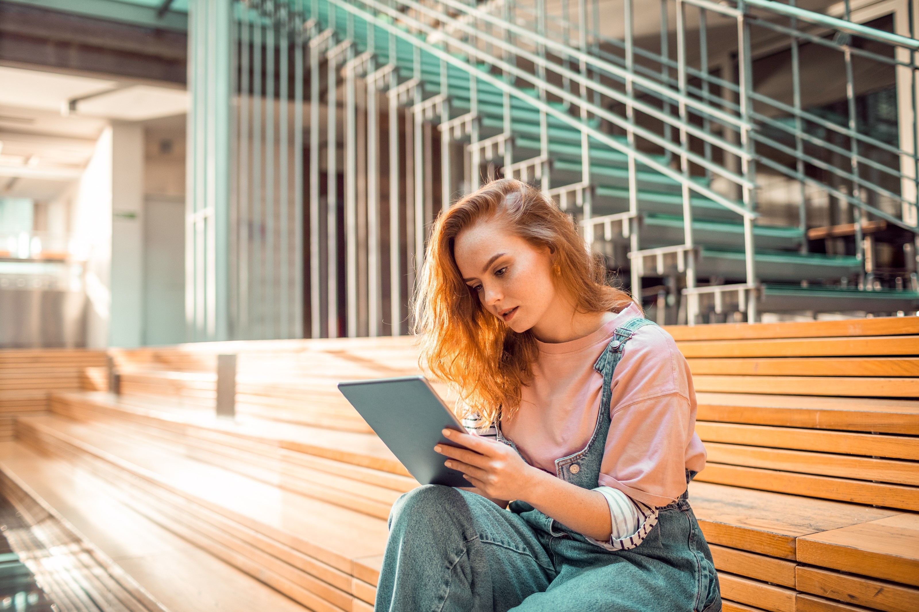 Eine junge Frau sitzt auf einer Bank und blickt konzentriert auf das Tablet in ihrer Hand